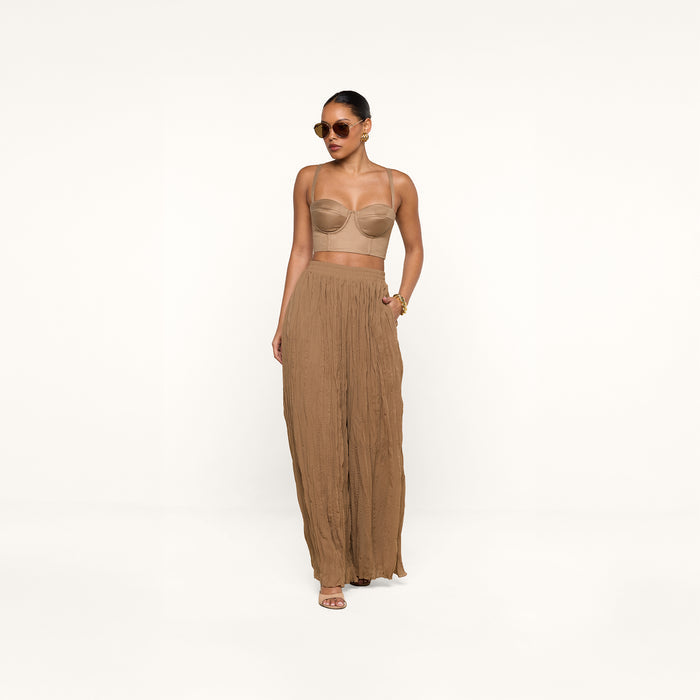 Wearing the Sonya Linen-Blend Bustier, a woman in sunglasses and high-waisted, wide-leg brown pants stands confidently against a white background with one hand in her pocket.