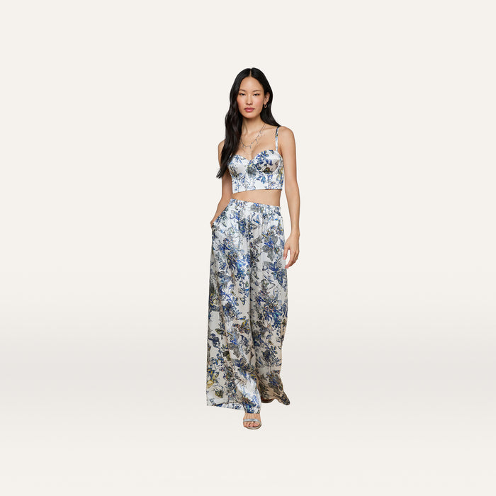 A woman stands with her hands in her pockets against a plain light background, wearing the Sonya Silk Bustier paired with matching wide-leg pants featuring a butterfly print.