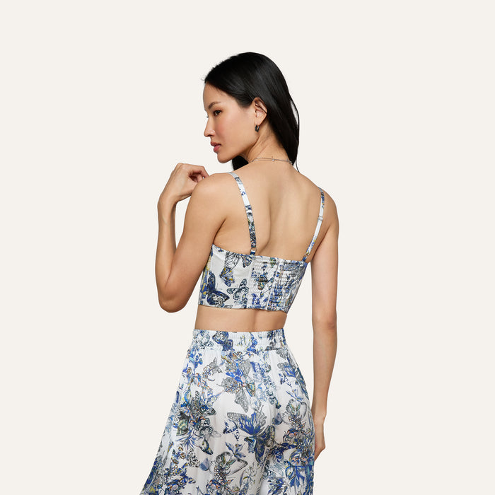 A woman is seen from the back, wearing the Sonya Silk Bustier and a matching skirt with a butterfly print. Her long dark hair cascades down against a neutral background.