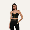 Wearing the Sophia Chain Bralette—a black crop top with gold chain straps and button accents that creates a structured silhouette—she pairs it with high-waisted black pants in stretch suiting fabric, finished with a gold chain belt, standing against a light background.