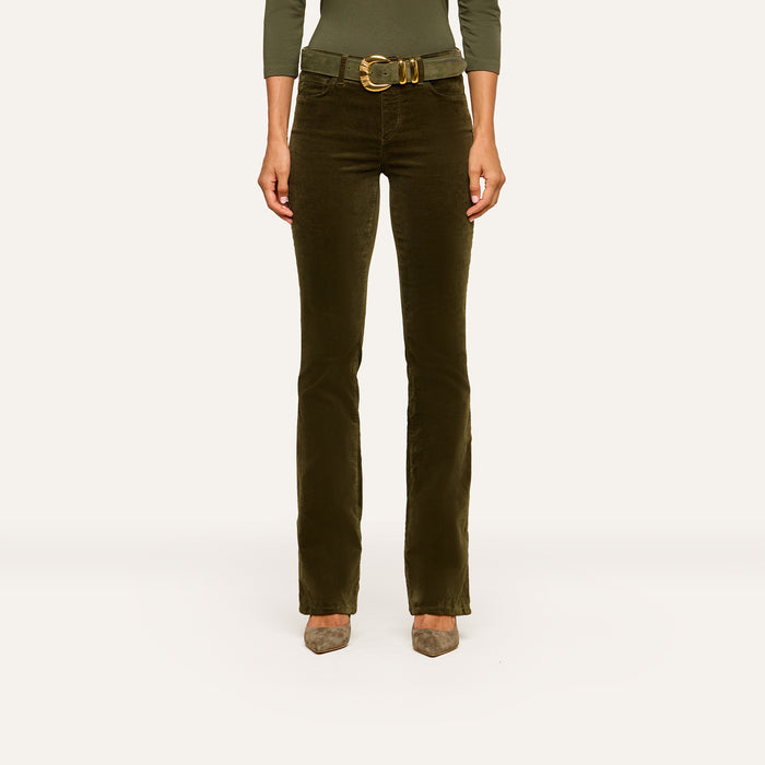 A person wearing the Stevie Velvet Jean, styled with a wide belt and taupe shoes, showcases its sleek high-rise silhouette and straight-leg fit against a plain light background. Only the lower torso and legs are visible.