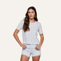 Wearing the Stormy Cropped Cotton Tee—a semi-relaxed fit top crafted from organic cotton—a woman with long brown hair pairs it with light denim shorts as she stands with her hands on her hips against a plain background.