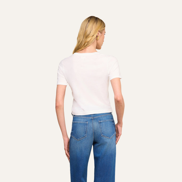 A person with long blonde hair is shown from behind, wearing the Stormy Cropped Cotton Tee in plain white and blue jeans against a light background.