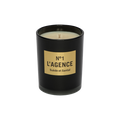 A black candle jar labeled Suède et Santal, adorned with a tan rectangular label and an unlit wick, is displayed against a plain white background. This elegant candle is crafted from a soy-blend wax and features the sophisticated scent of sandalwood.