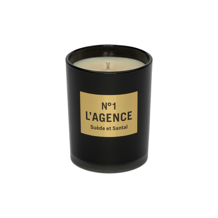A black candle jar labeled Suède et Santal, adorned with a tan rectangular label and an unlit wick, is displayed against a plain white background. This elegant candle is crafted from a soy-blend wax and features the sophisticated scent of sandalwood.