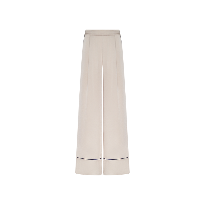 The Tavia Trouser is a wide-leg, high-waisted style crafted from cream-colored satin, featuring subtle waistband detailing and a thin dark horizontal stripe near the hem of each leg. These luxe loungewear pull-on trousers are showcased against a plain white background.