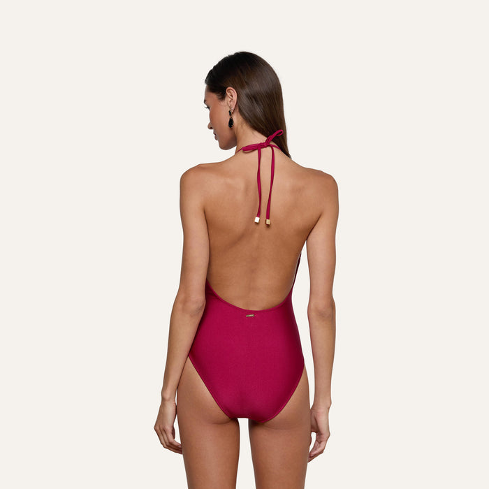 A woman, seen from behind, models the Terra One-Piece Swimsuit—featuring a bold red color with lace trim and gold accents—against a simple, light background.