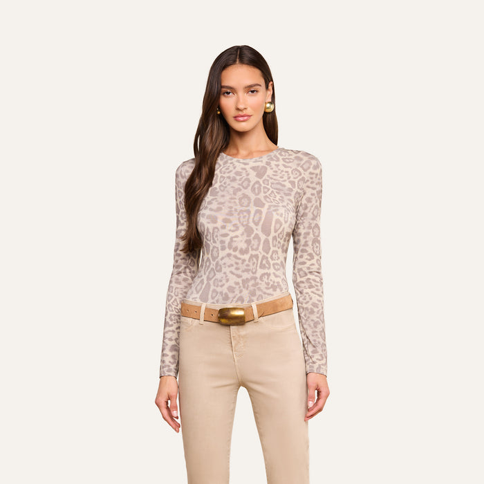 A woman wears the Tess Long Sleeve Tee—a slim-fit, beige leopard-print top—paired with tan pants and a tan belt with a gold buckle, standing against a plain light background.