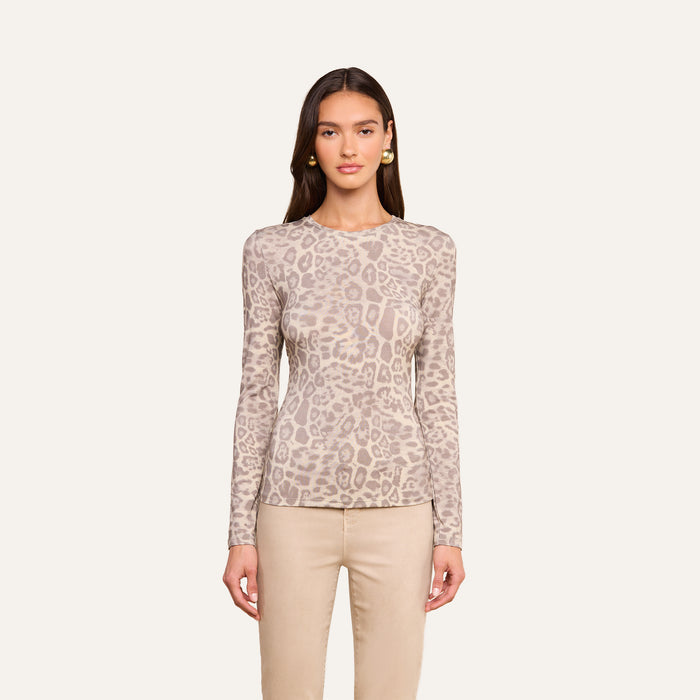 A woman wears the Tess Long Sleeve Tee, featuring a slim fit and subtle grey leopard print, paired with beige pants and set against a plain off-white background.