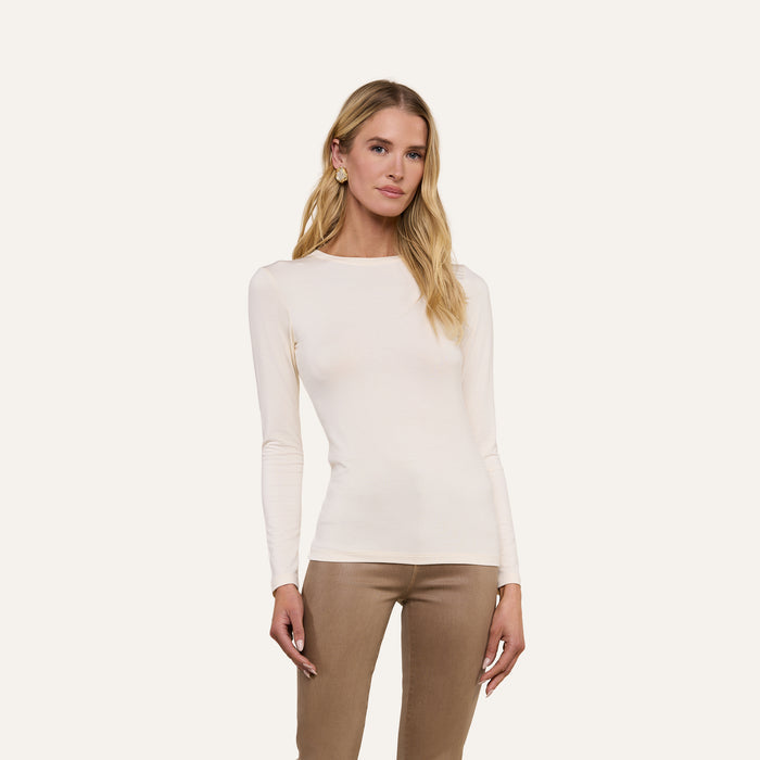 A woman with long blonde hair wears the Tess Long Sleeve Tee in a slim fit, paired with light brown pants, standing against a plain light background.