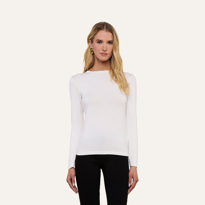 A woman with long blonde hair wears the Tess Long Sleeve Tee in white and black pants, standing facing forward against a plain, light background.