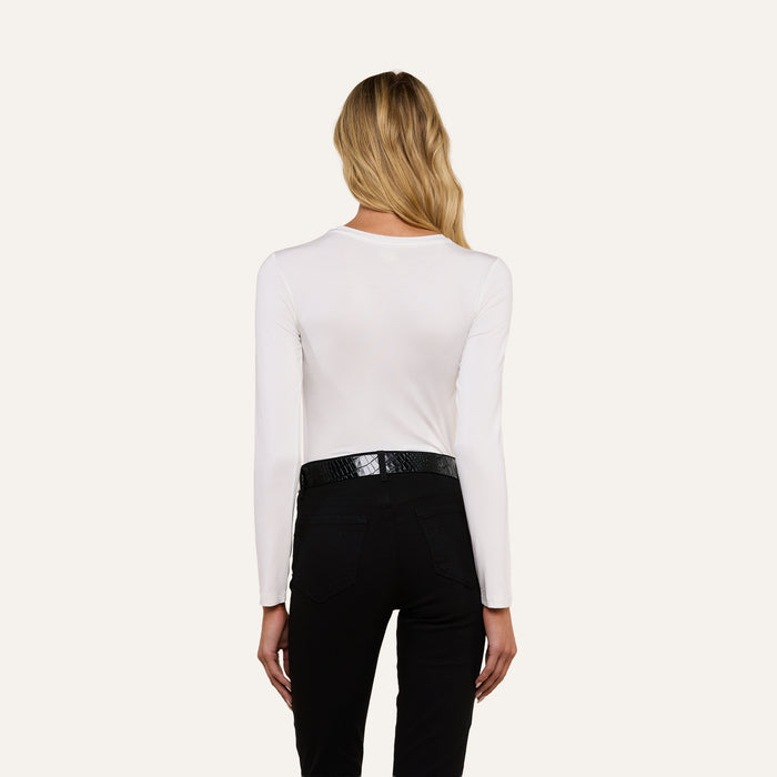 A person with long, wavy blond hair is shown from the back, wearing the Tess Long Sleeve Tee, a black belt, and black pants against a plain light background.