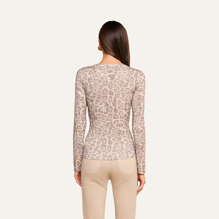 A woman with straight brown hair is shown from the back against a plain light background wearing the Tess Long Sleeve Tee—a slim fit, long-sleeve grey leopard print top—paired with beige pants.