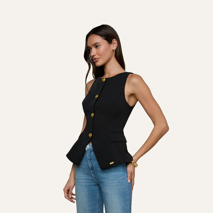 A woman wearing the Tessa Vest—a sleeveless suit vest with gold buttons—paired with blue jeans stands against a plain light background.