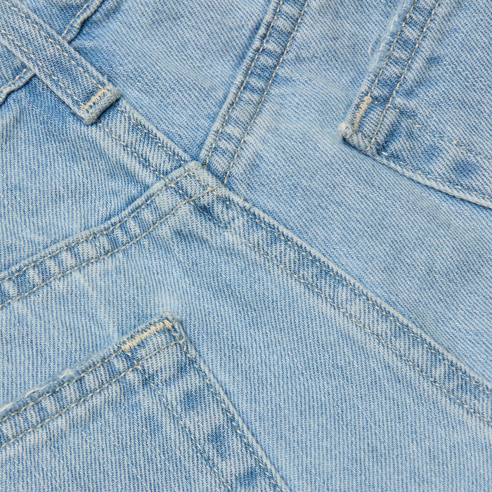 Close-up of the Teya Low-Rise Jean Short in a light blue wash, showcasing overlapping seams, pockets, and visible stitching details. The image highlights the texture, color, and structure of the denim material.