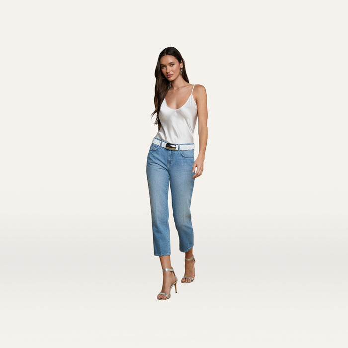 A woman in a white camisole, Thalina Cropped Stovepipe Jean in a light blue wash, and beige heels walks forward against a plain white background.