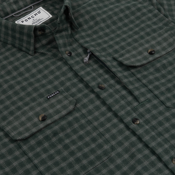 Close-up of The Acadia green plaid shirt with buttoned chest pockets and Poncho Outdoors label detail.