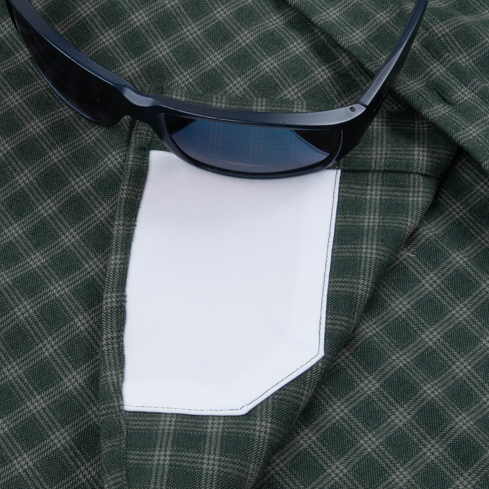 Close-up of The Acadia shirt showing green plaid fabric, white pocket detail, and black sunglasses resting on top
