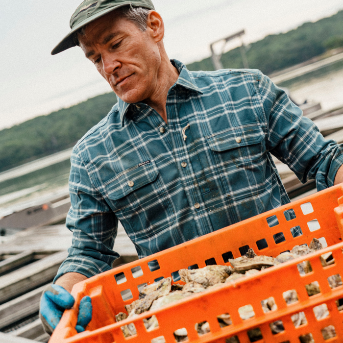 The Codfather plaid shirt worn by a man carrying a crate of oysters outdoors