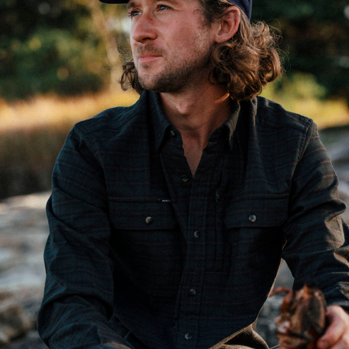 The Gloucester dark plaid shirt worn by a man outdoors beside a forest stream