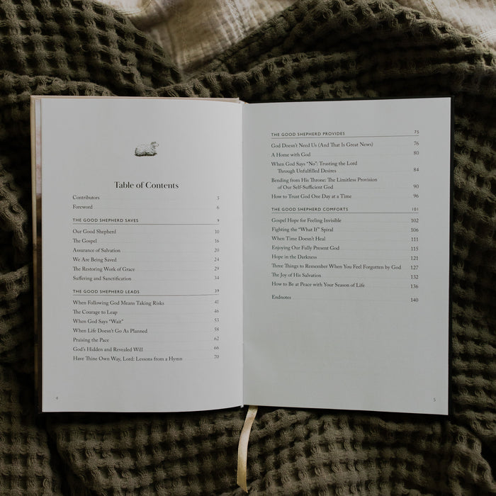 The Good Shepherd opened to the Table of Contents page laying on a green waffle styled blanket on another creme blanket