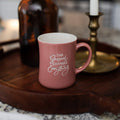 The Gospel Changes Everything Primrose Mug siting on a wooden round tray with a bronze candle and a brown glass bottle behind it
