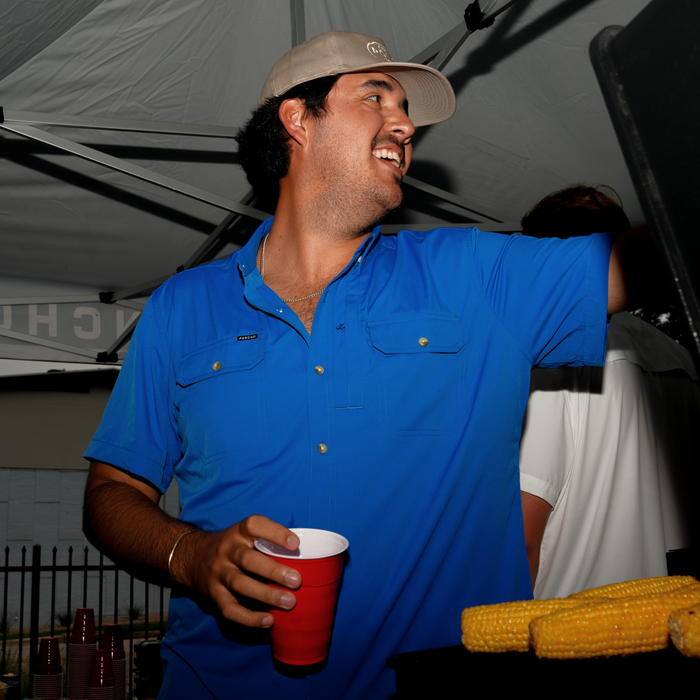 The Grandstand blue button up shirt worn by a smiling man serving food at an outdoor gathering