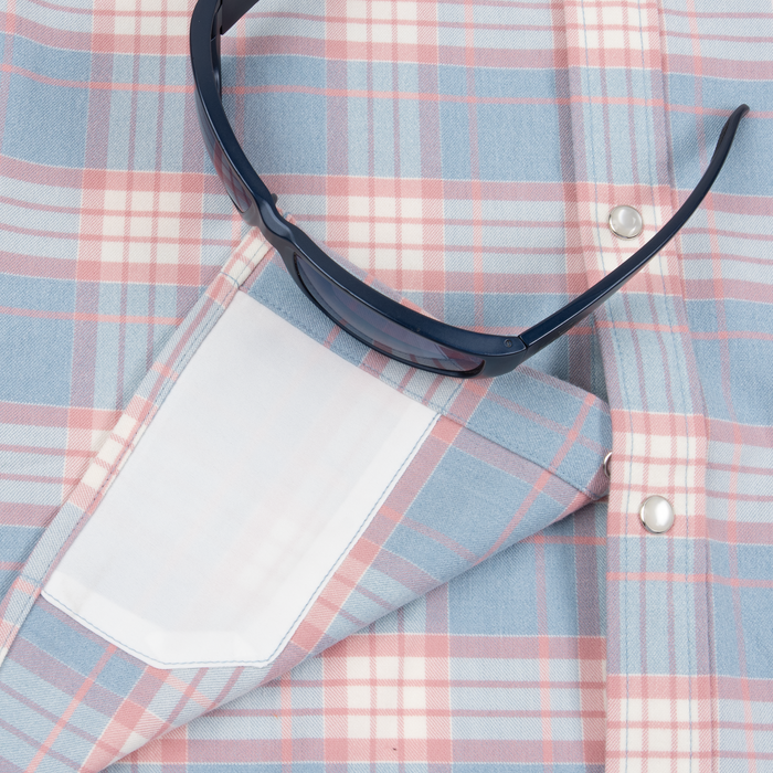 Close-up of folded plaid fabric shirt in pastel blue and pink with sunglasses resting on top, showcasing The Pacific City shirt design.