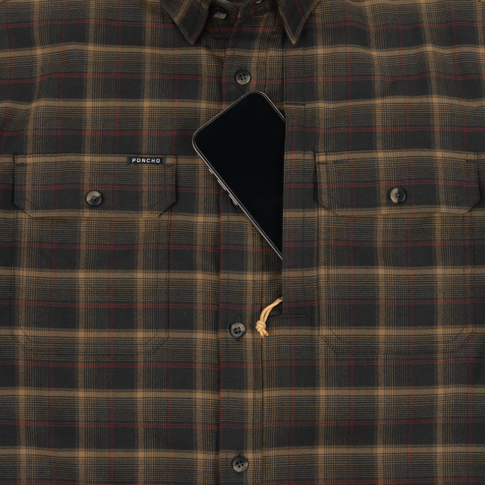 Close-up of The Rusty Saw plaid shirt with buttoned chest pockets and a smartphone partially tucked into one pocket