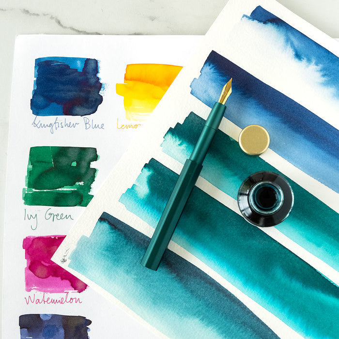 The Pocket Fountain Pen in Ivy shown with an open bottle of fountain pen inks and a selection of ink colour swatches on paper