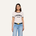 Woman with long brown hair wearing the Tommie Crewneck Tee in white, paired with light blue jeans and a black belt with a gold buckle, standing against a plain light background.
