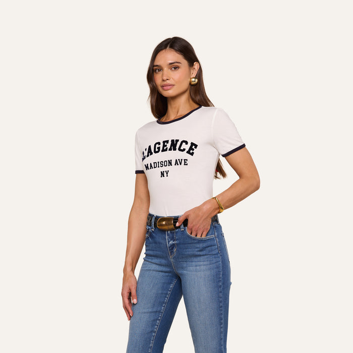 A woman in a relaxed fit white Tommie Crewneck Tee made from Supima cotton and blue jeans stands against a plain background, looking forward with one hand in her pocket.