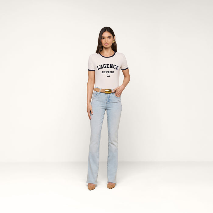 A woman stands against a white background wearing a Tommie Crewneck Tee, light blue jeans, a tan belt, and tan heels. She faces forward with arms relaxed at her sides in a relaxed fit ensemble.