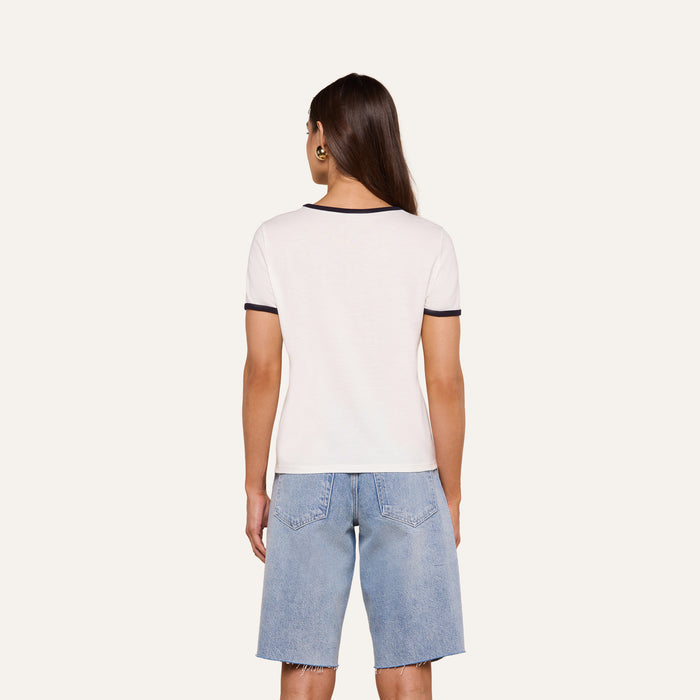Wearing the relaxed fit Tommie Crewneck Tee in white with dark trim, a person faces away against a plain light background, paired with light blue knee-length denim shorts.