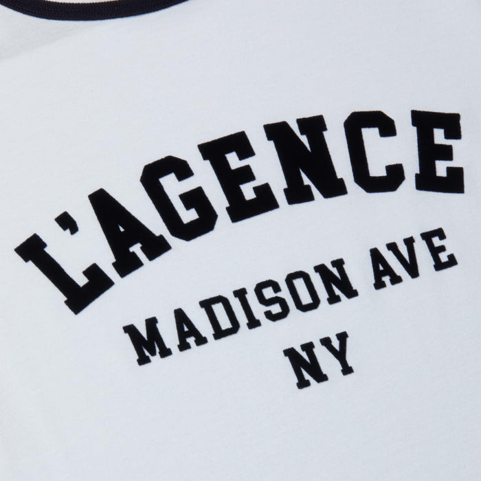 Close-up of a white Tommie Crewneck Tee made from Supima cotton, featuring bold black text reading LAGENCE and smaller text beneath reading MADISON AVE NY.