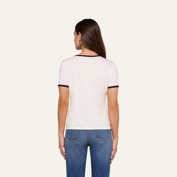 A woman with long brown hair stands facing away, wearing the Tommie Crewneck Tee—crafted from soft Supima cotton in a relaxed fit—paired with blue jeans against a plain light background.