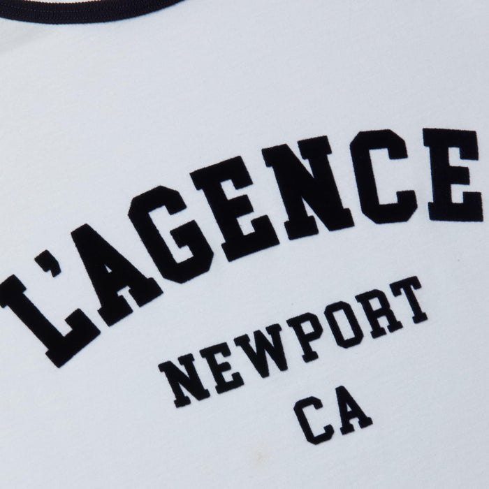 Introducing the Tommie Crewneck Tee: a white ringer tee featuring black text with “LAGENCE” in large letters and “NEWPORT CA” in smaller print underneath. Crafted from soft Supima cotton, it offers a relaxed fit for all-day comfort.