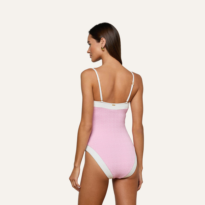 A woman with long brown hair models the Tory Bandeau One-Piece Swimsuit in pink bouclé fabric with white trim, shown from the back against a plain light background.