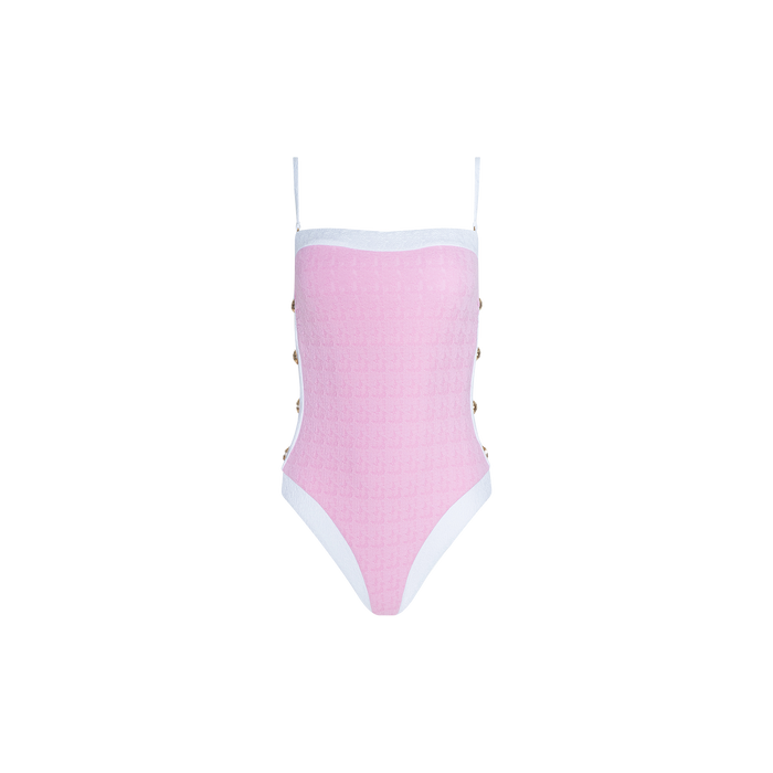 The Tory Bandeau One-Piece Swimsuit is a pink one-piece featuring thin white shoulder straps and white trim. Metallic button details decorate the sides, while textured bouclé fabric adds interest throughout. The swimsuit is photographed against a plain white background.