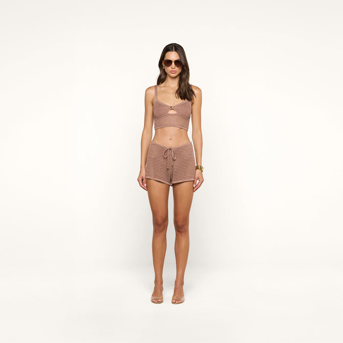 A woman stands facing forward against a plain white background, wearing sunglasses and the Tracy Bralette Top, styled with matching high-waisted shorts featuring a brown checkered pattern and subtle metal accents.