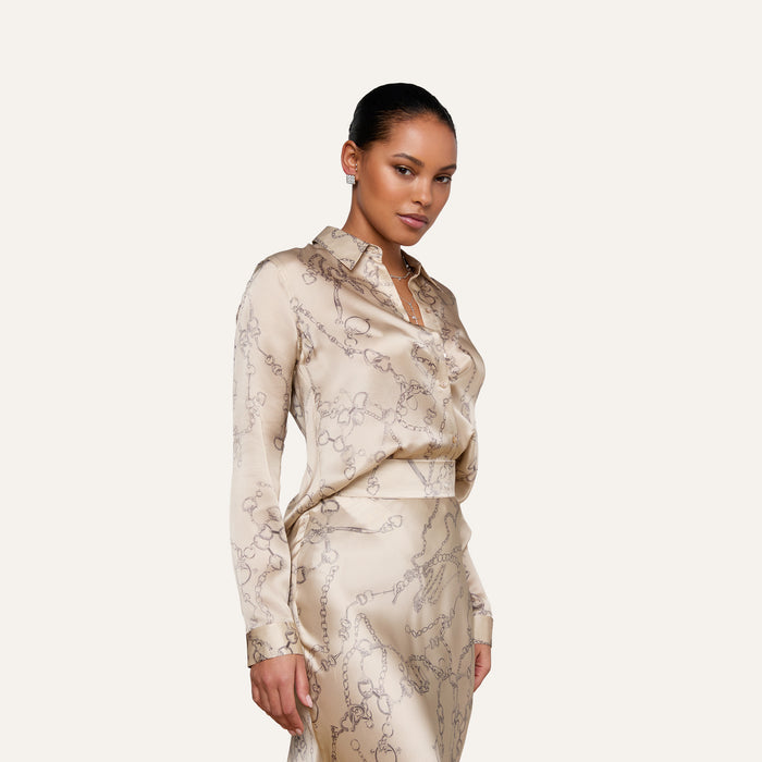 A woman wearing a beige chain print satin skirt and a matching Tyler Silk Blouse stands against a light background, looking confidently at the camera.