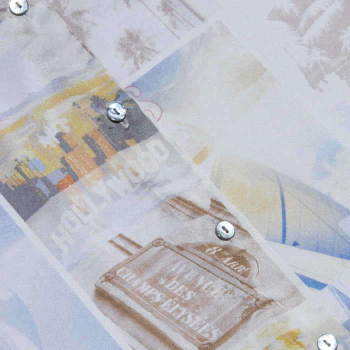 A close-up of the Tyler Silk Blouse shows its silk charmeuse fabric adorned with faded images of palm trees, cityscapes, and a Hollywood sign, all accented by decorative metallic studs scattered across the design.