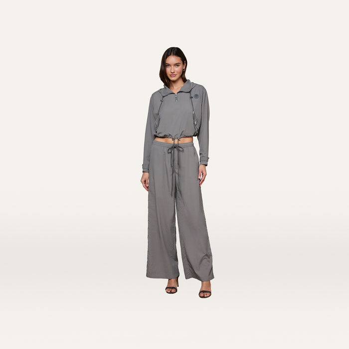 A woman stands against a plain white background, wearing a gray, long-sleeve cropped jacket and matching Valkyrie Snap Pant with black open-toe heels.