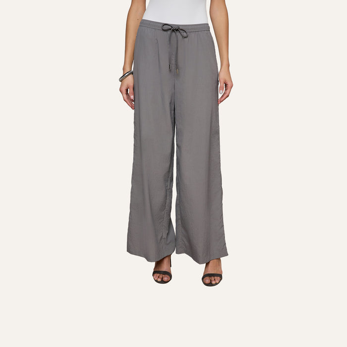 A person wearing loose, gray Valkyrie Snap Pants with a relaxed fit, paired with black heeled sandals and a white top. The image is cropped at the shoulders.