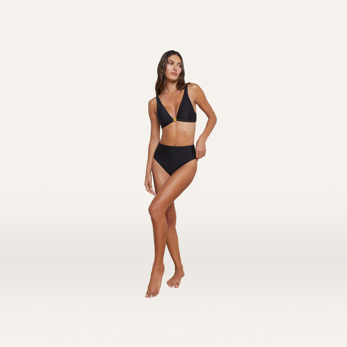 A woman stands on one leg against a plain white background, wearing the Vanessa High-Waisted Bikini Bottom with moderate coverage and a V-neck bikini top.