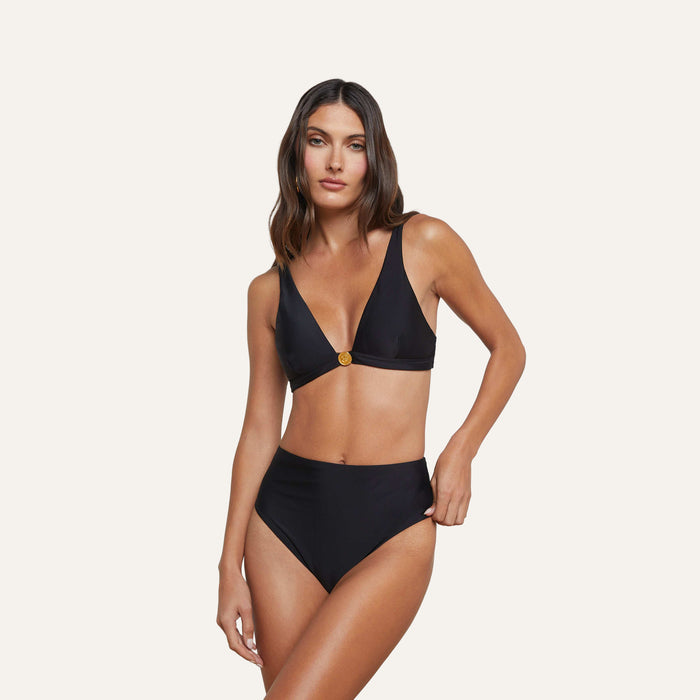 A woman with long brown hair models the Vanessa High-Waisted Bikini Bottom—a versatile black bikini set featuring a V-neck top and high-waisted bottom for moderate coverage—against a plain light background.