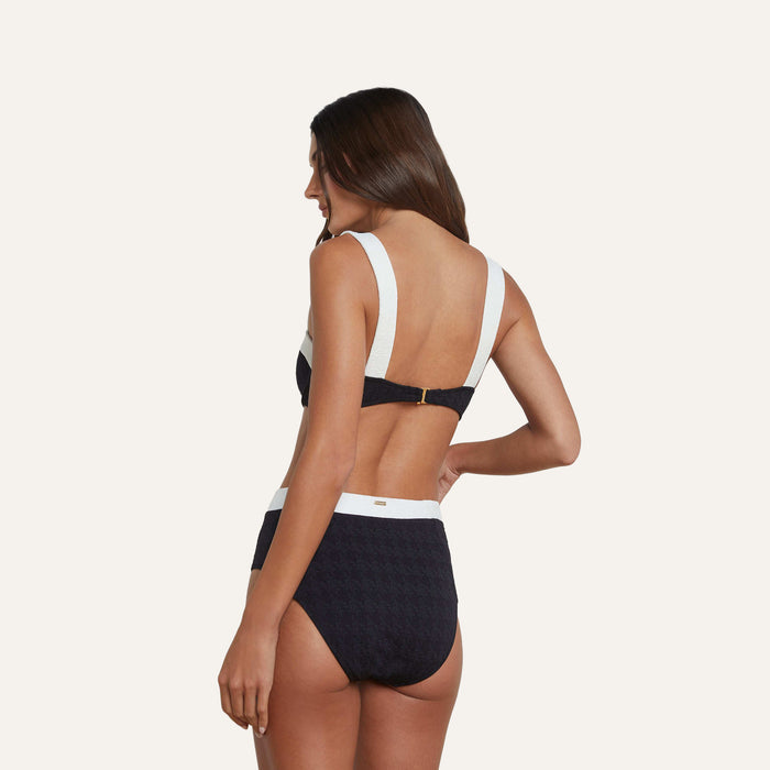 A woman with long brown hair is shown from the back against a plain light background wearing the Vanessa High-Waisted Bikini Bottom—a black and white textured bouclé piece adorned with gold buttons.