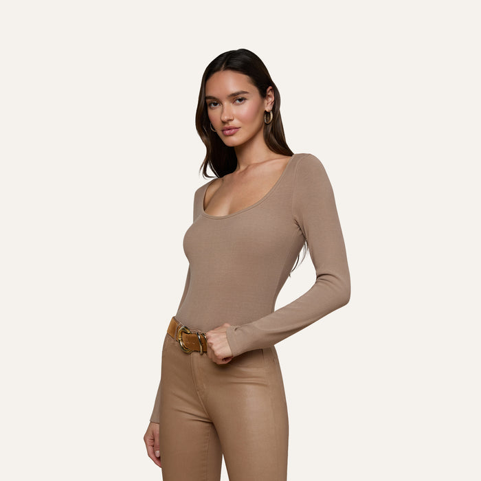 Wearing the Vanya Scoopneck Top, a woman stands against a plain light background paired with tan belted pants.