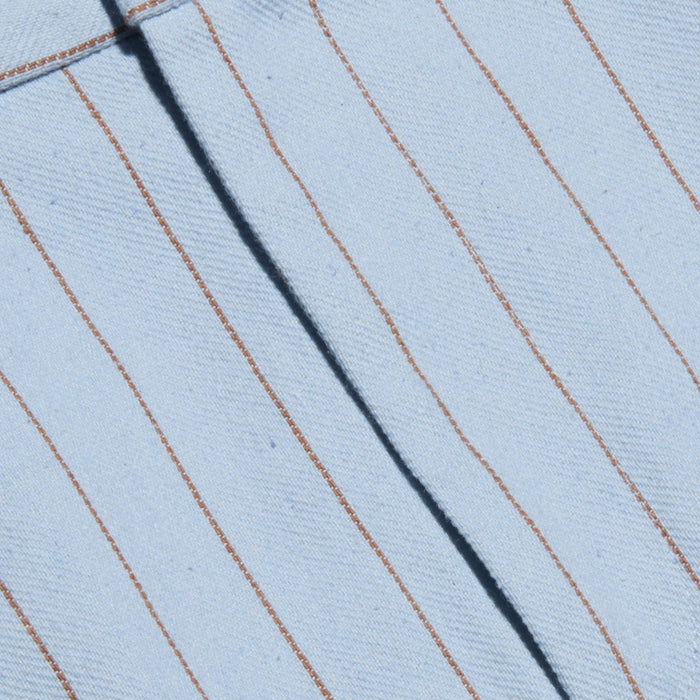 Close-up of the Vera Pinstriped Mini Skirt, crafted from a light blue cotton blend fabric featuring thin, evenly spaced vertical brown pinstripes and a visible seam running diagonally across the tailored silhouette.