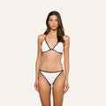A woman faces forward against a plain light background, wearing the Violet String Bikini Bottom—a white bikini bottom with black trim and moderate coverage—paired with a matching top.